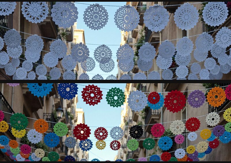 Dos fotografías de la misma calle estrecha vista hacia arriba, con adornos redondos de papel recortado colgados en hileras entre los balcones. Arriba, todos los adornos son blancos y azul pálido. Abajo, los mismos adornos son rojos, verdes, amarillos, azules, naranjas y morados.